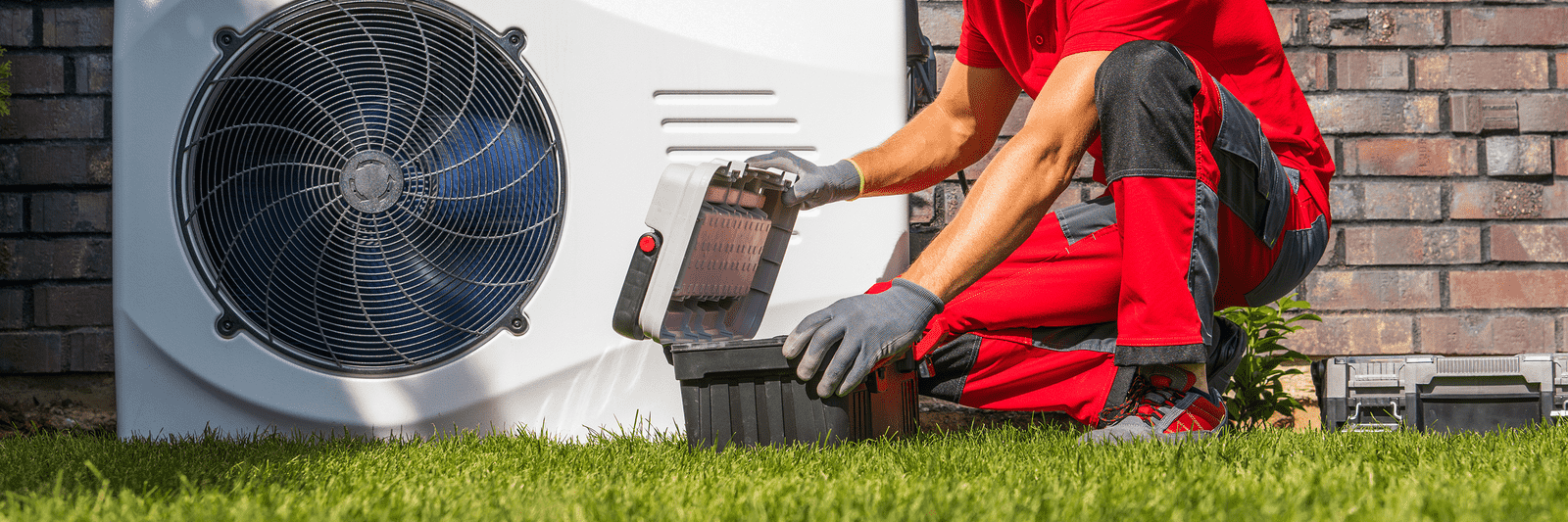 Technician servicing an outdoor heat pump with a toolbox at his side