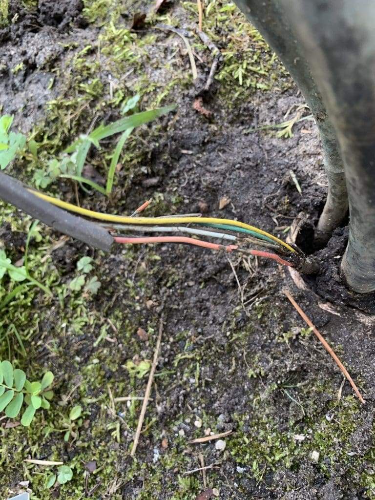 Thermostat wire with damaged insulation running through the soil beside an outdoor unit’s line set