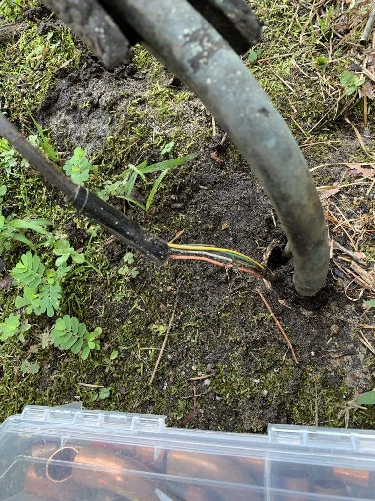 Thermostat wire with damaged insulation running through the soil beside an outdoor unit’s line set